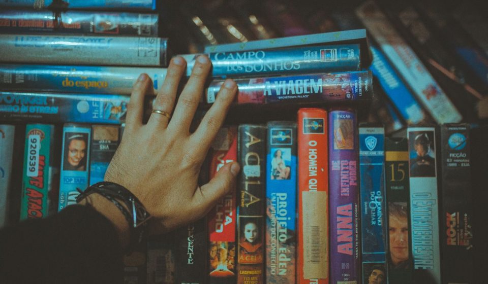 A hand reaching for a classic VHS tape from a colorful vintage collection indoors.